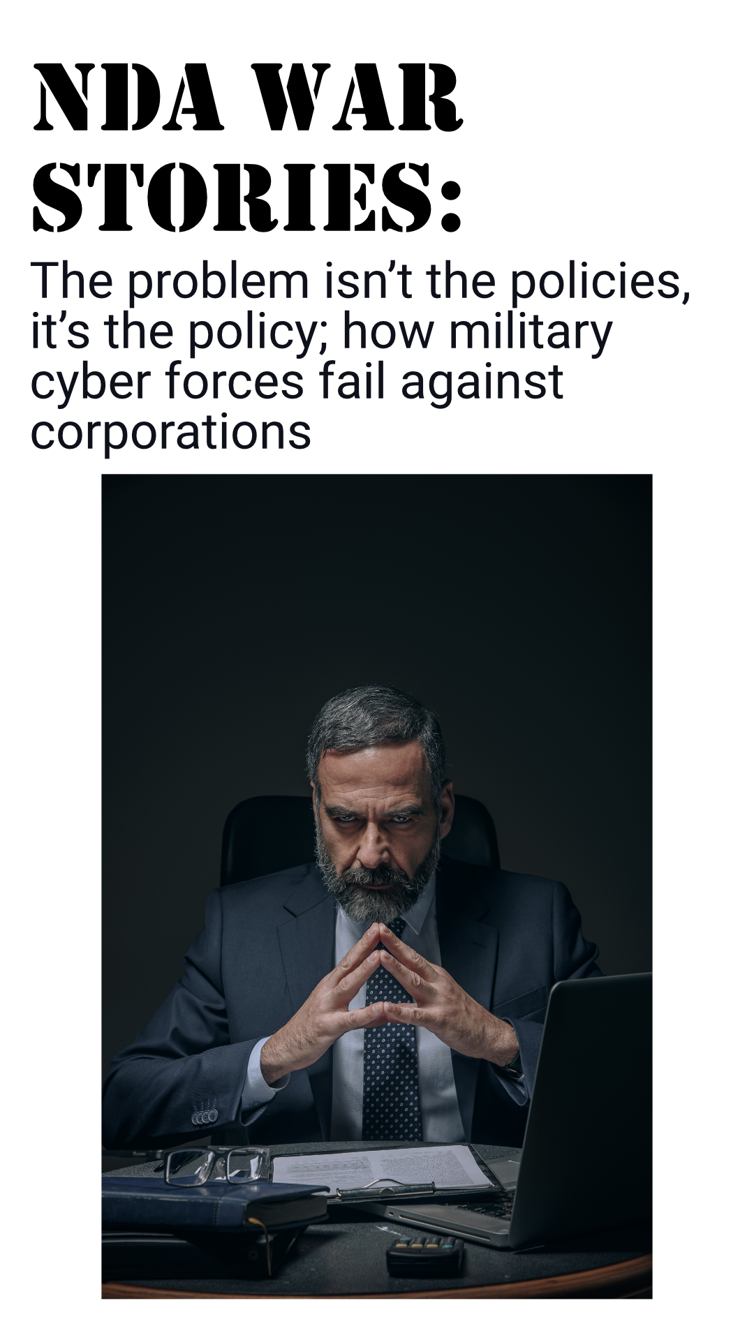 Evil business person glares directly over a desk with a laptop. The scowl of the man intesifies with a piercing gaze as he rests his elbows over the desk while arching his fingers together in sign of superiority.
